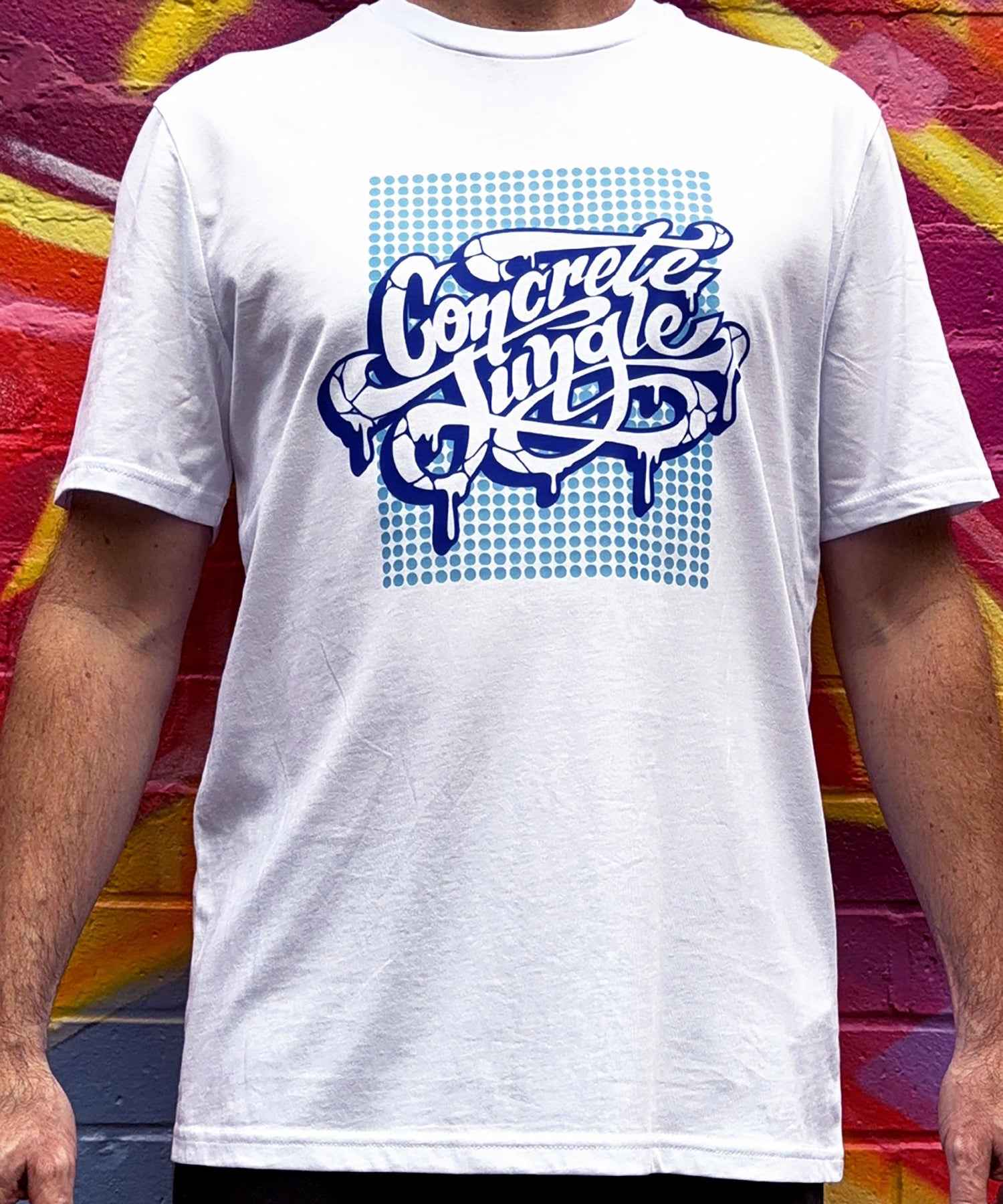 White t-shirt with 'Concrete Jungle' design worn by a person in front of a colorful mural.